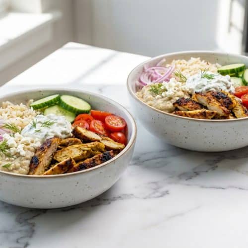 A colorful chicken shawarma bowl featuring jasmine rice, hummus, and fresh salad, topped with pan-seared chicken strips with crispy edges.