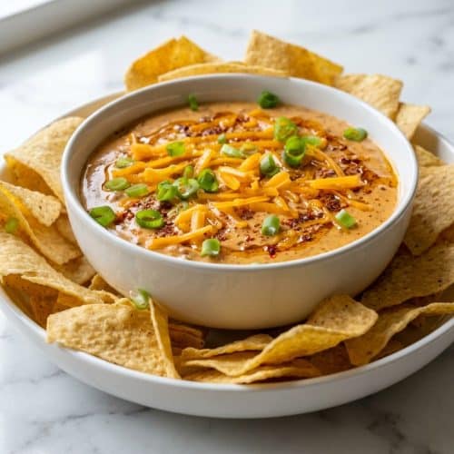 Bowl of hot Cream Cheese and Chili Queso Dip drizzled with red oil from the spice bloom technique surrounded by tortilla chips.