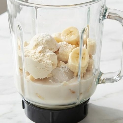 A tall glass of a creamy vanilla protein shake recipe, made extra thick with cauliflower and topped with a banana slice.