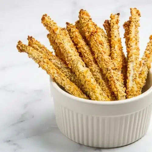 Golden Crispy Baked Eggplant Fries stacked next to marinara sauce. Pre-sweating and cornstarch ensure a perfectly crunchy bite.