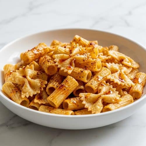 Golden brown farfalle pasta chips recipe coated in bloomed spiced oil and parmesan cheese piled in a serving bowl.