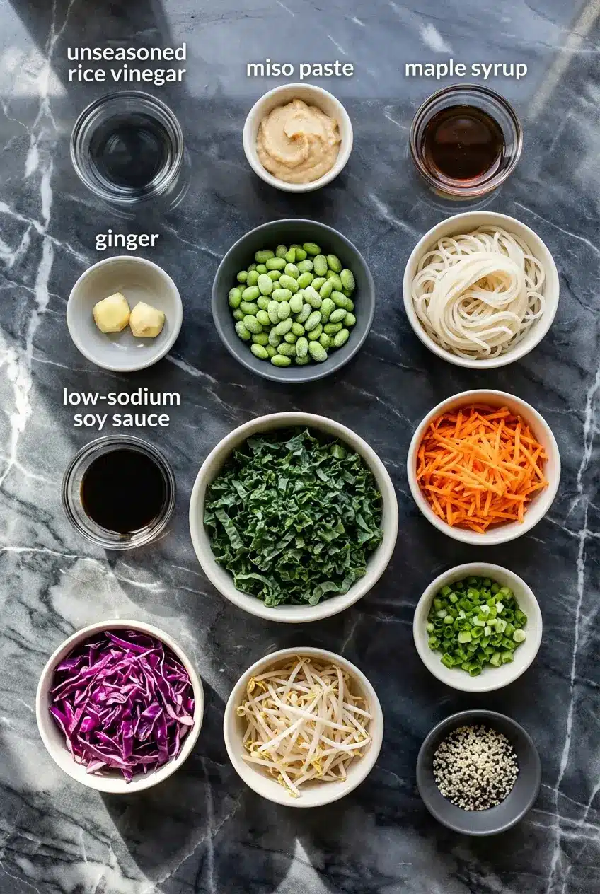 Flat lay of ingredients for edamame rice noodle salad including dry rice noodles, miso paste, tamari, and mukimame.