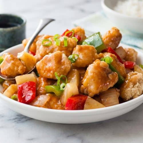 A bowl of Sweet and Sour Chicken with a visibly crispy coating from a rice flour blend, tossed with bell peppers and pineapple.
