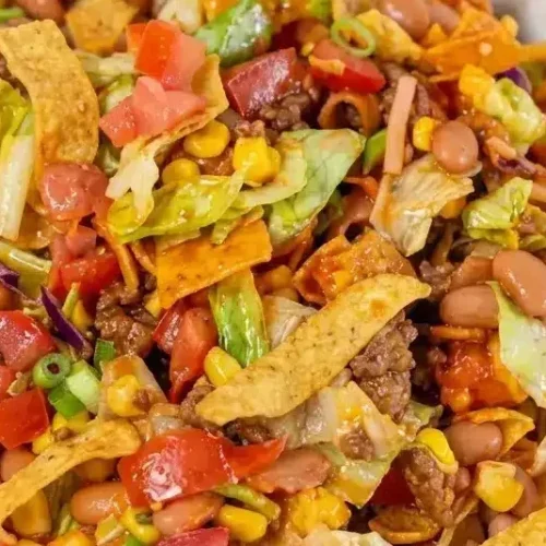 A large bowl of frito taco salad topped with charred corn, fresh greens, and tossed in lime-spiked Catalina dressing.