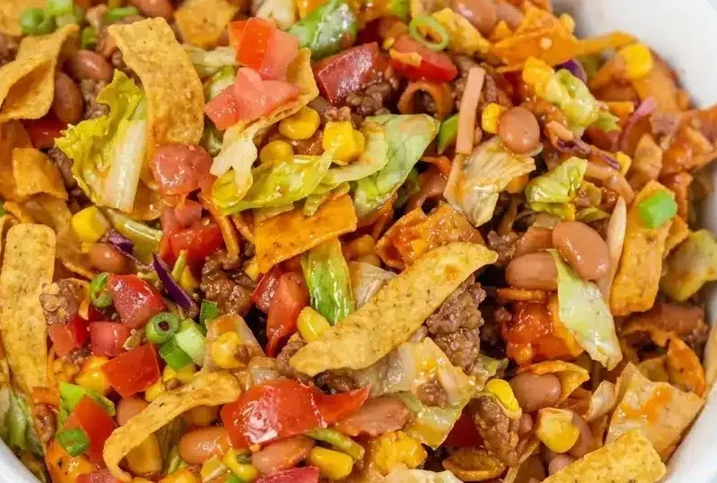 A large bowl of frito taco salad topped with charred corn, fresh greens, and tossed in lime-spiked Catalina dressing.