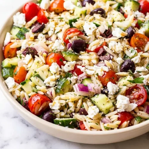 A bowl of greek orzo salad recipe tossed with cherry tomatoes, cucumbers, and a creamy whipped feta and olive brine emulsion.