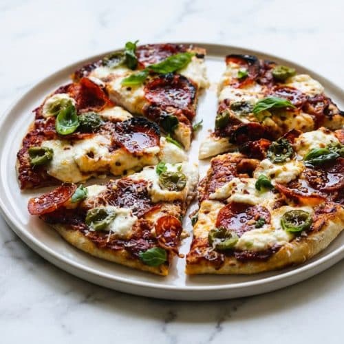 Sliced hot honey pizza recipe topped with pepperoni, fresh mozzarella, and a glossy brown butter Calabrian chili emulsion.
