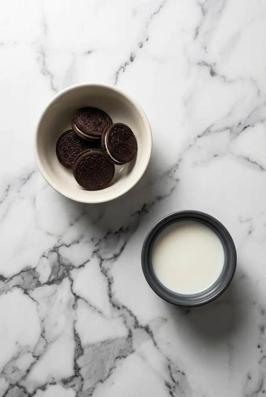 Overhead view of ingredients for a 2 Ingredient Oreo Mug Cake, showing Oreo cookies, milk, baking powder, and dark chocolate.