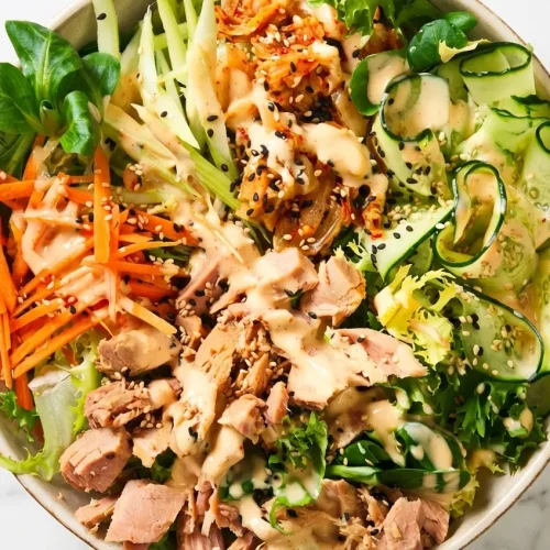 Bowl of vibrant kimchi salad drizzled with creamy miso tahini dressing and topped with crushed toasted peanuts.