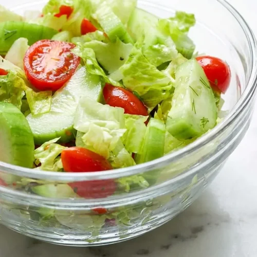A fresh bowl of lettuce tomato and cucumber salad tossed in a vibrant tomato-juice vinaigrette with red wine vinegar.