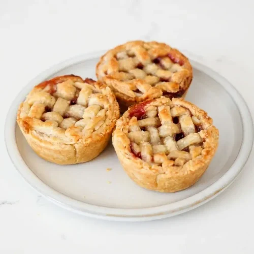 Golden mini cherry pies with a brown butter lattice crust, cardamom-spiced filling, and sparkling coarse sugar.