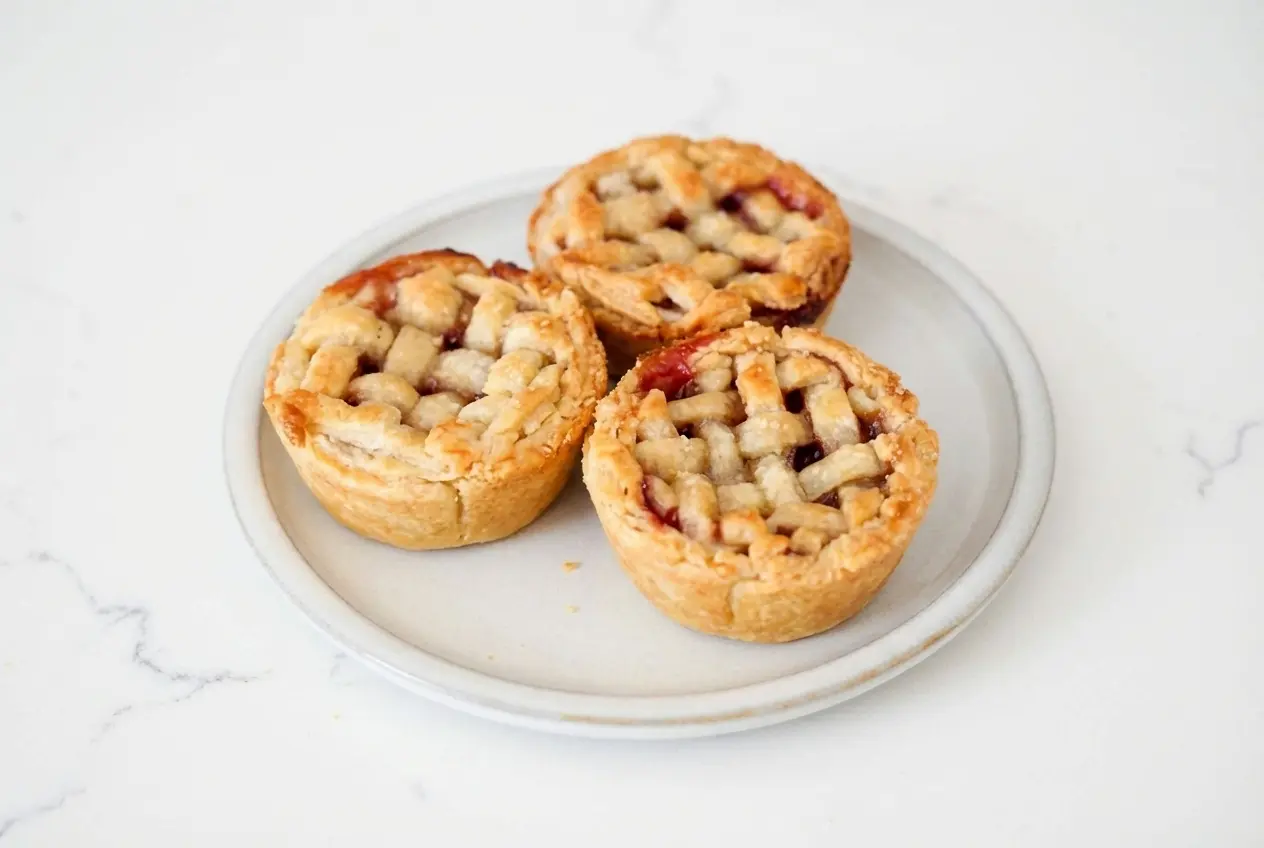 Golden mini cherry pies with a brown butter lattice crust, cardamom-spiced filling, and sparkling coarse sugar.