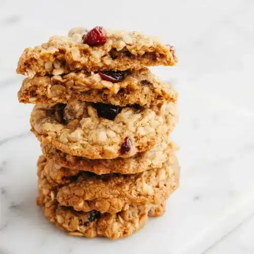Chewy oatmeal cranberry cookies made with brown butter and plump, orange juice-soaked berries stacked on a cooling rack.