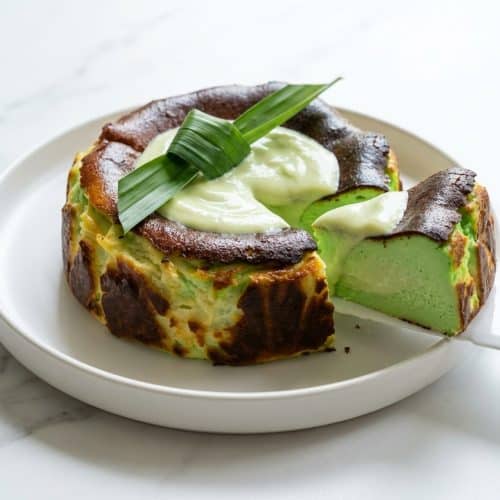 A slice of pandan basque cheesecake with a dark burnt top and vibrant green, coconut cream infused custard center on a plate.