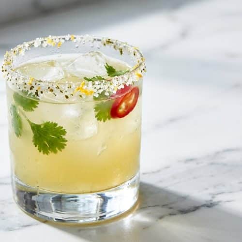 Icy Picante Cocktail in a rocks glass featuring a coriander-citrus salt rim and a slice of fresh Fresno chili.