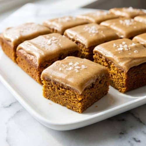 A sheet pan of perfectly cut pumpkin bars with caramel frosting, finished with a delicate sprinkle of flaky sea salt.