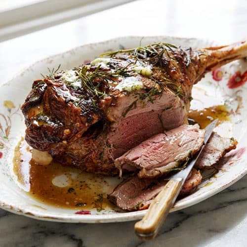 Golden brown roast lamb leg with gravy carved to reveal tender pink meat, seasoned with savory anchovy butter and herbs.