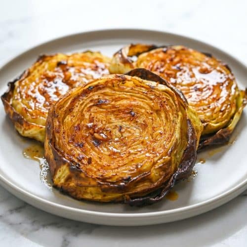 Thick slices of green cabbage brushed with an umami-miso butter glaze, baked until tender for this roasted cabbage steaks recipe.