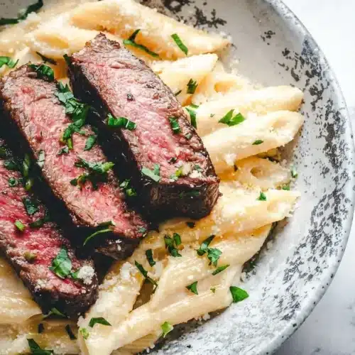 Plated steak pasta recipe featuring medium-rare sliced ribeye over creamy noodles, finished with a rich balsamic drizzle.