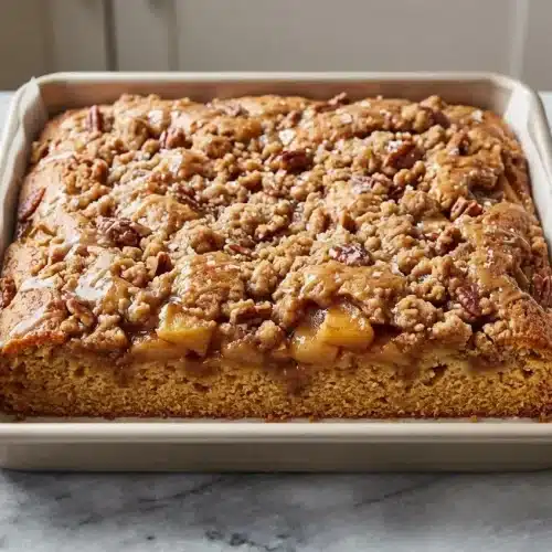 A square slice of Apple Crisp Coffee Cake with a thick, nutty brown butter and toasted pecan streusel topping, drizzled with glaze.