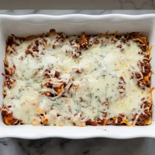 A golden-brown high protein lasagna in a baking dish, with a slice removed to show the creamy whipped cottage cheese layers.