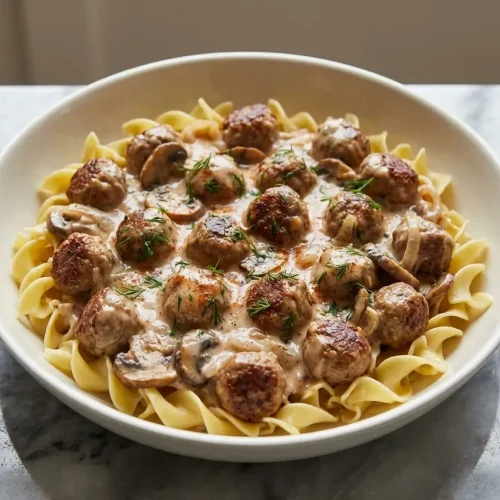 A bowl of creamy Meatball Stroganoff with tender meatballs in a rich, paprika-infused sauce, served over egg noodles with fresh dill.
