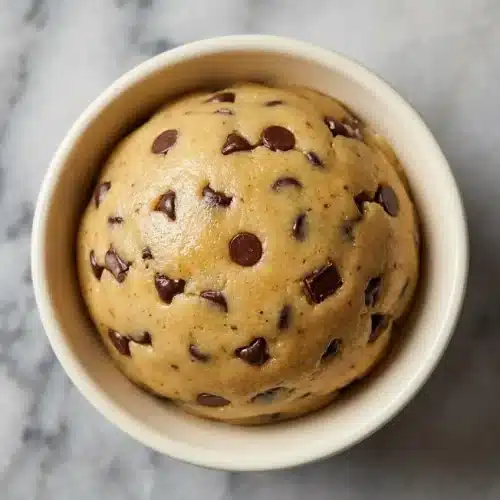 A scoopable bowl of protein cookie dough recipe made with rich browned butter and toasted oat flour, dotted with chocolate chips.