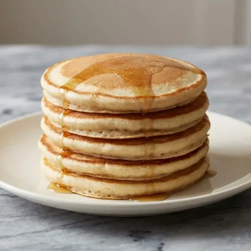 A tall, fluffy stack of protein vegan pancakes made with vegan buttermilk, topped with fresh berries and a drizzle of maple syrup.