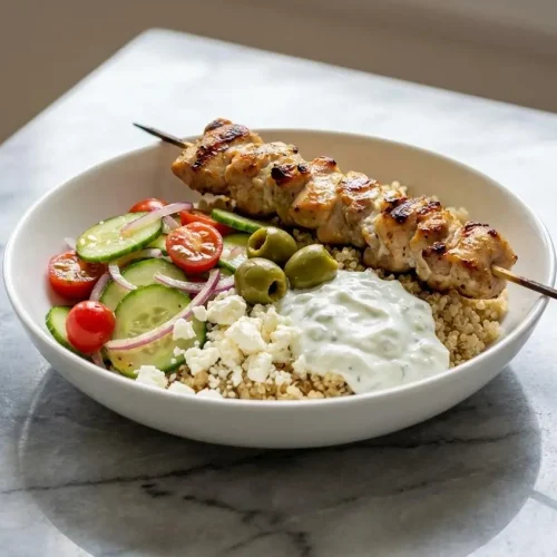 A chicken gyro bowl with smoky paprika-spiced chicken, quinoa, fresh cucumbers, tomatoes, feta cheese, and a dollop of tzatziki.