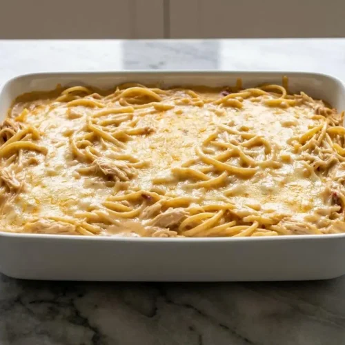A 9x13 baking dish of homemade chicken spaghetti recipe with a bubbly, golden-brown cheddar and Gruyère cheese crust.