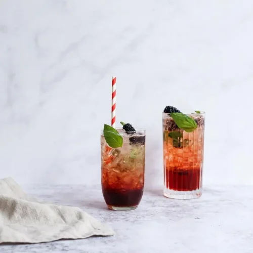 A tall, refreshing glass of Blackberry Sage Iced Tea filled with ice cubes and garnished with a fresh lime wedge.