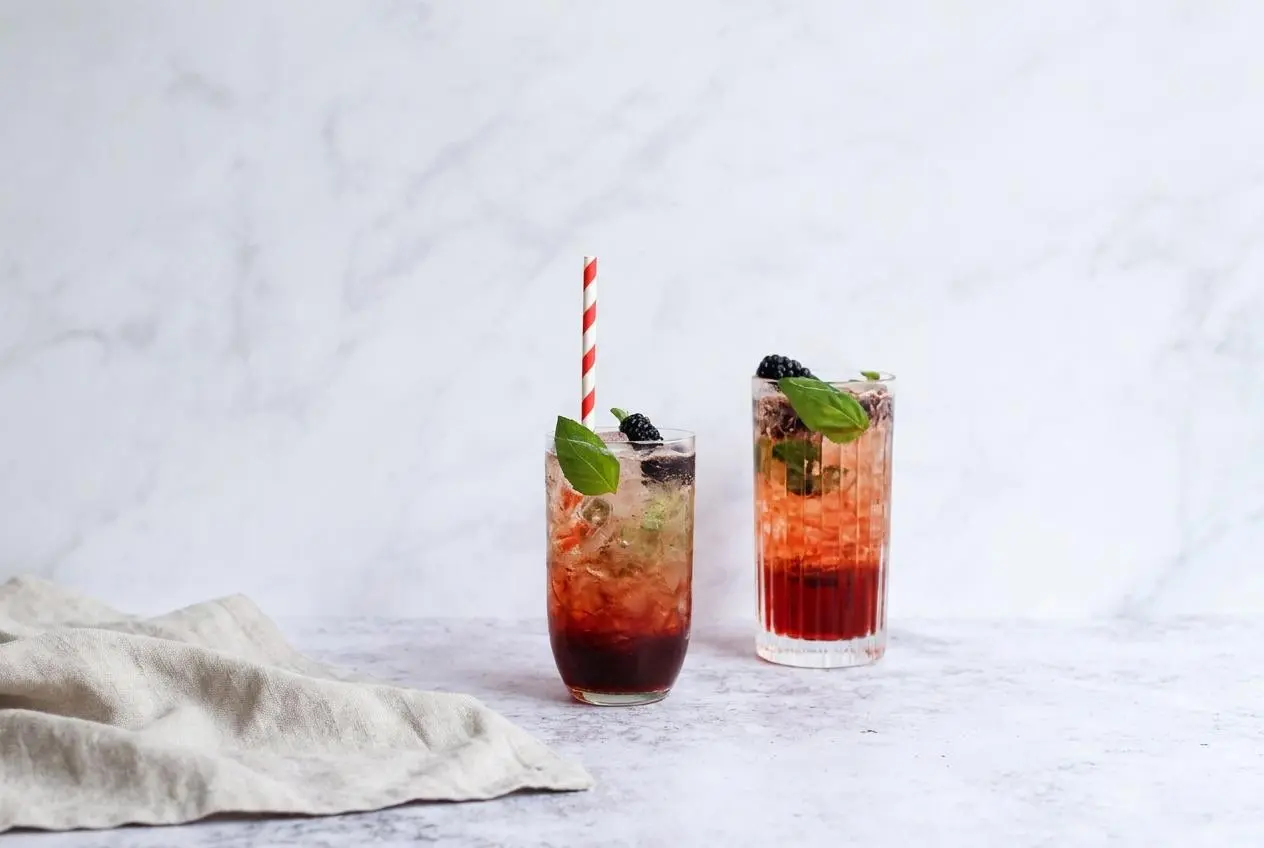 A tall, refreshing glass of Blackberry Sage Iced Tea filled with ice cubes and garnished with a fresh lime wedge.