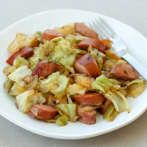 A black skillet filled with Cabbage and Sausage, showing smoky, browned kielbasa and tender-crisp cabbage with a glossy finish.