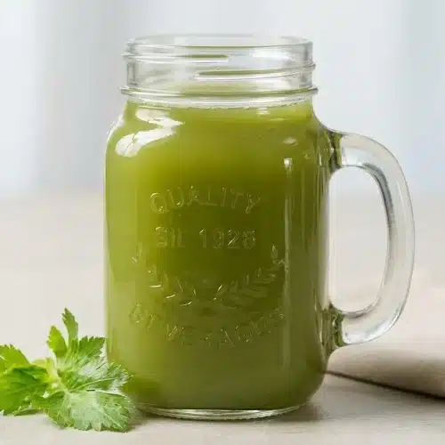 A tall glass of freshly made celery juice recipe, showing its pale green color and light natural froth on top.