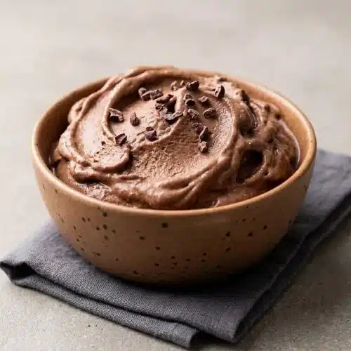 A bowl of creamy chocolate protein ice cream with a perfect scoop taken out, showing its smooth, rich texture.