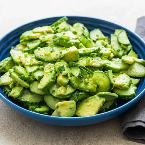 A large white bowl of cucumber avocado salad, showing creamy sliced avocado and crisp cucumber with a light, glossy dressing.