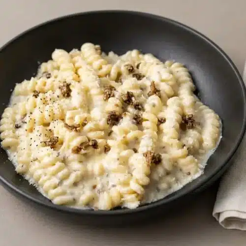 A white bowl of creamy Truffle Pasta, with a glossy Parmesan sauce clinging to fusilli corti bucati pasta.