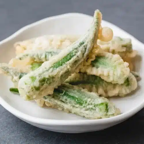 A serving of okra tempura with a light, crispy golden batter, piled in a rustic bowl.
