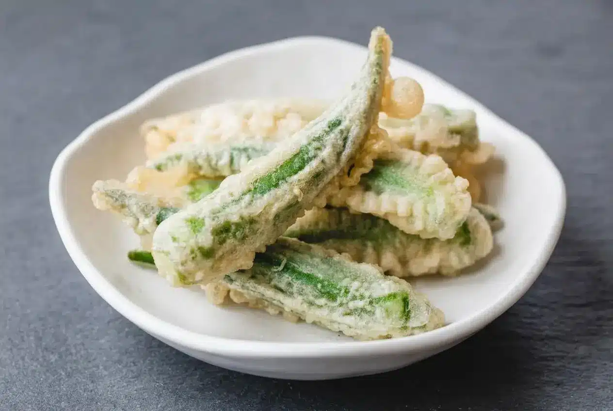 A serving of okra tempura with a light, crispy golden batter, piled in a rustic bowl.