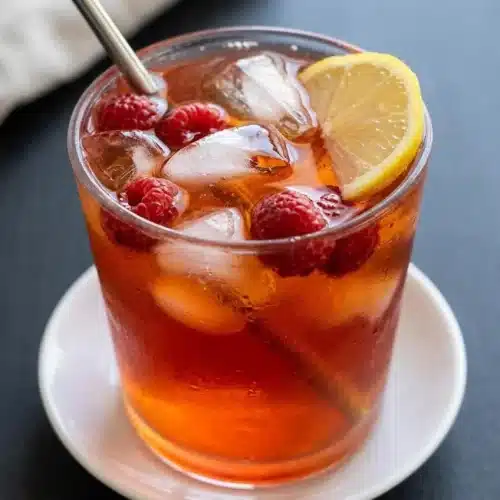 A tall glass of Earl Grey Raspberry Iced Tea filled with ice cubes and fresh raspberries, showing its refreshing, clear ruby color.
