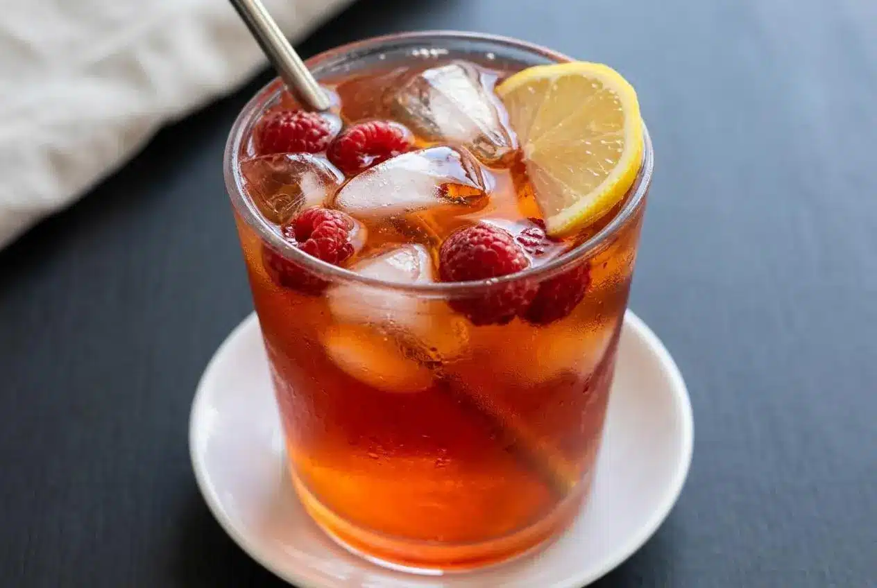 A tall glass of Earl Grey Raspberry Iced Tea filled with ice cubes and fresh raspberries, showing its refreshing, clear ruby color.