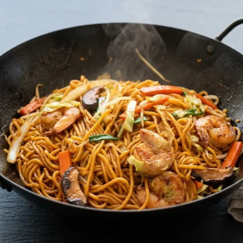 A serving of shrimp lo mein with a glossy sauce, tender shrimp, and chewy noodles in a dark bowl.