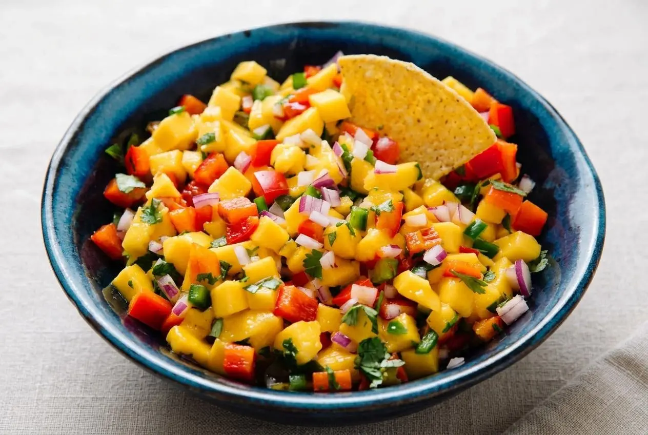 A white bowl filled with fresh, chunky mango salsa, showing diced mango, red bell pepper, red onion, and cilantro.