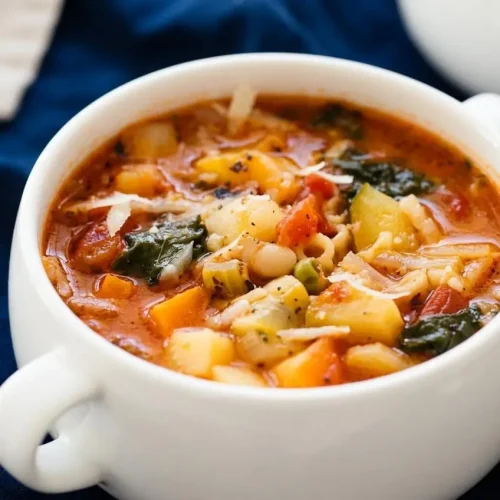 A rustic bowl of hearty Minestrone Soup filled with vegetables, beans, and pasta in a rich tomato broth, garnished with grated Parmesan