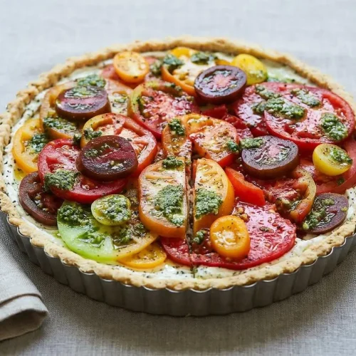 A rustic heirloom tomato tart recipe with a golden, flaky crust and a creamy goat cheese filling, with one slice removed.