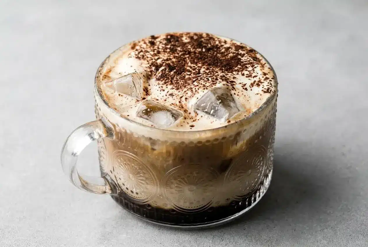 Iced Tiramisu Latte in a tall glass showing distinct layers and a creamy mascarpone foam topping dusted with cocoa.