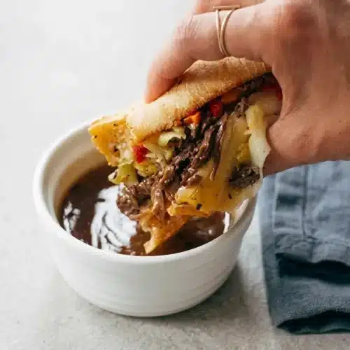 An Instant Pot Italian Beef sandwich on a crusty hoagie roll, overflowing with tender shredded beef, melted provolone, and giardiniera.