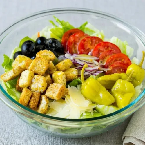 A large serving bowl of Olive Garden salad recipe, featuring crisp lettuce, red onion, tomatoes, and croutons in a creamy Italian dressing.