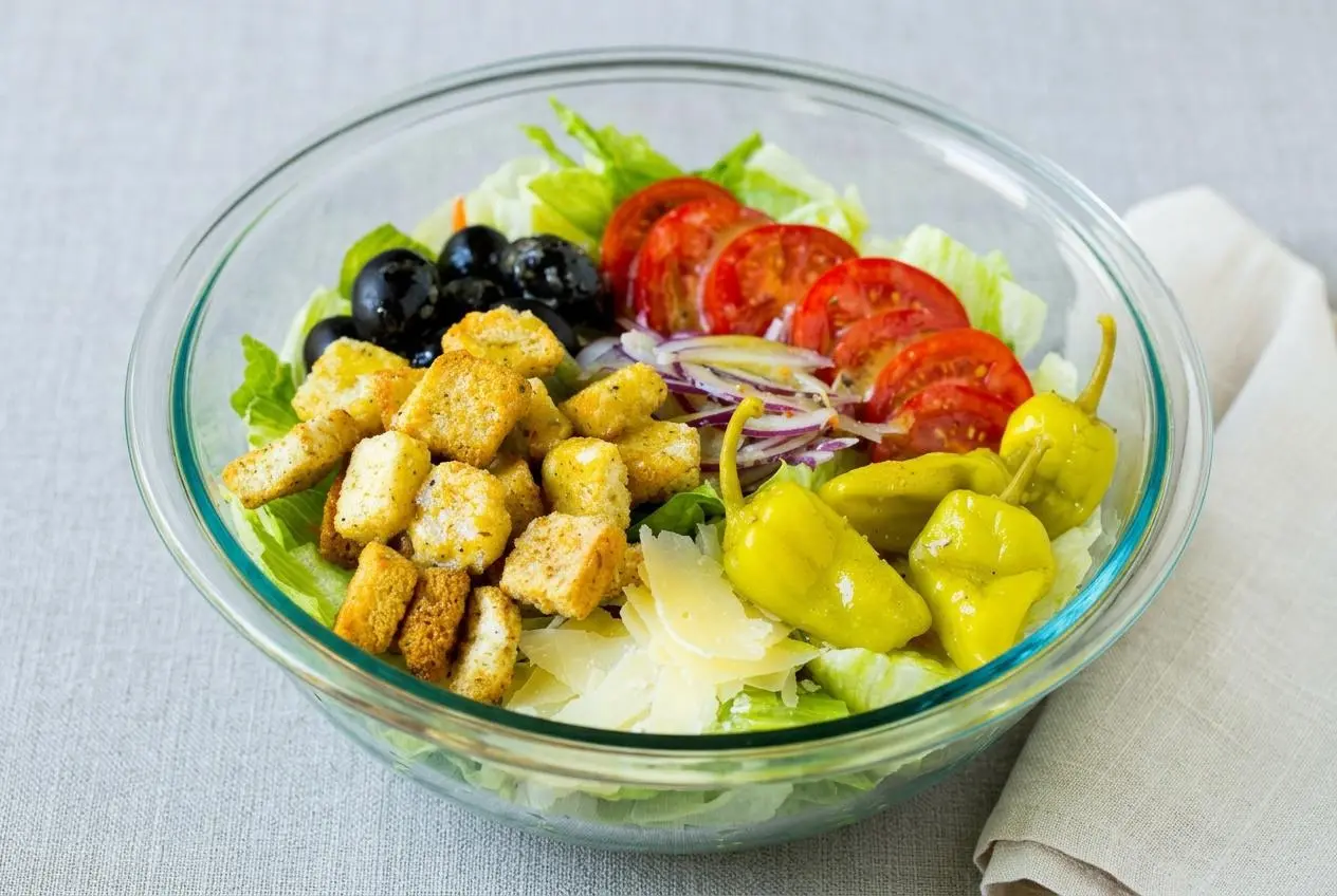 A large serving bowl of Olive Garden salad recipe, featuring crisp lettuce, red onion, tomatoes, and croutons in a creamy Italian dressing.