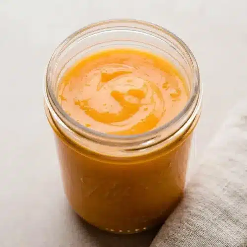 A small white bowl filled with the finished orange curd recipe, showing its silky, bright orange surface with a spoon resting inside.